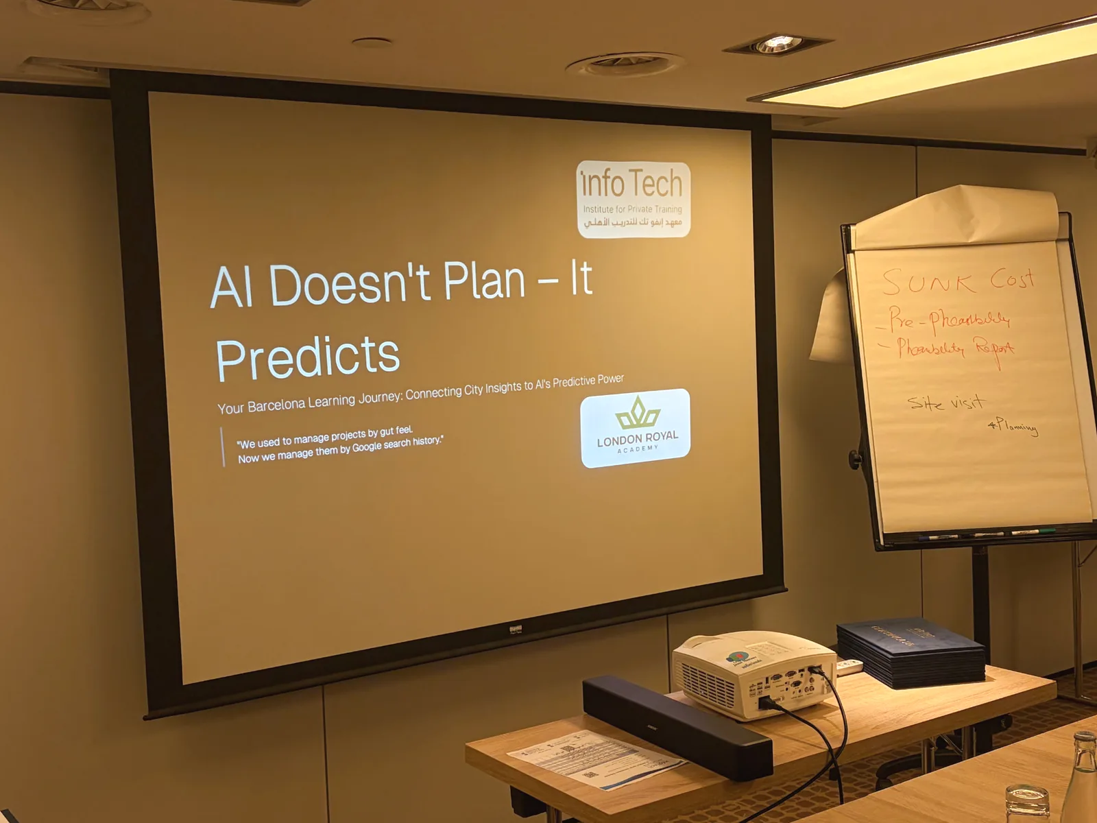 A London Royal Academy AI session in progress, with the slide “AI doesn’t plan – it predicts” beside a flipchart of notes